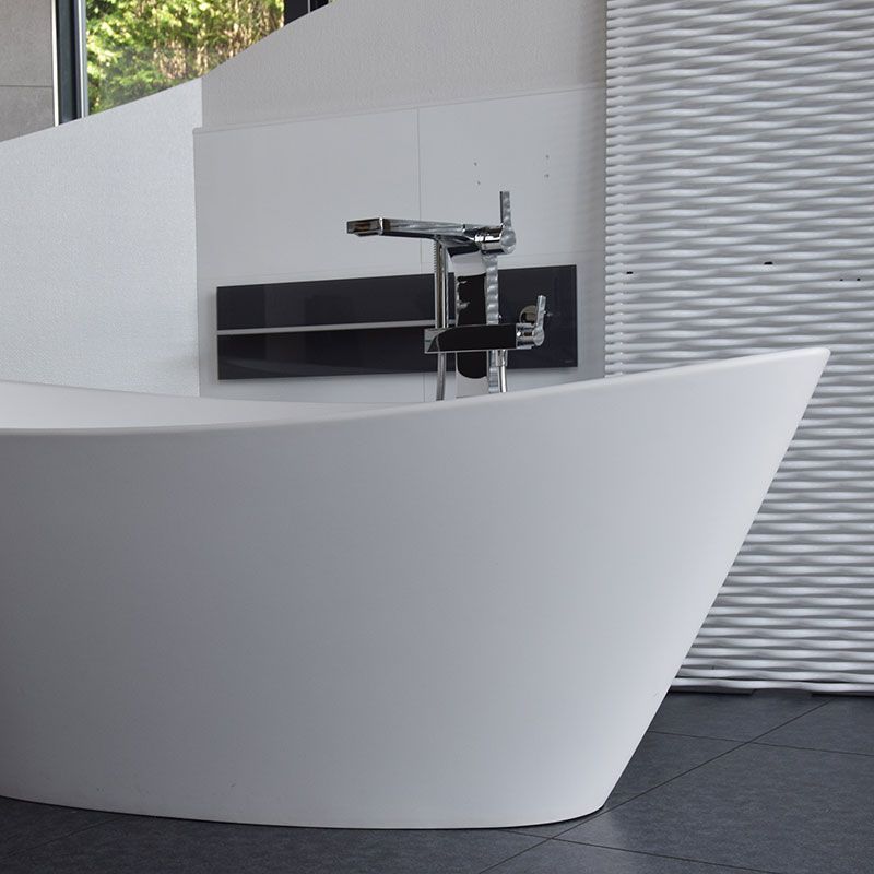 Freistehende ovale Badewanne in Weiß mit bodenstehender Chrom-Standarmatur vor einer weißen Wellenstruktur-Wand