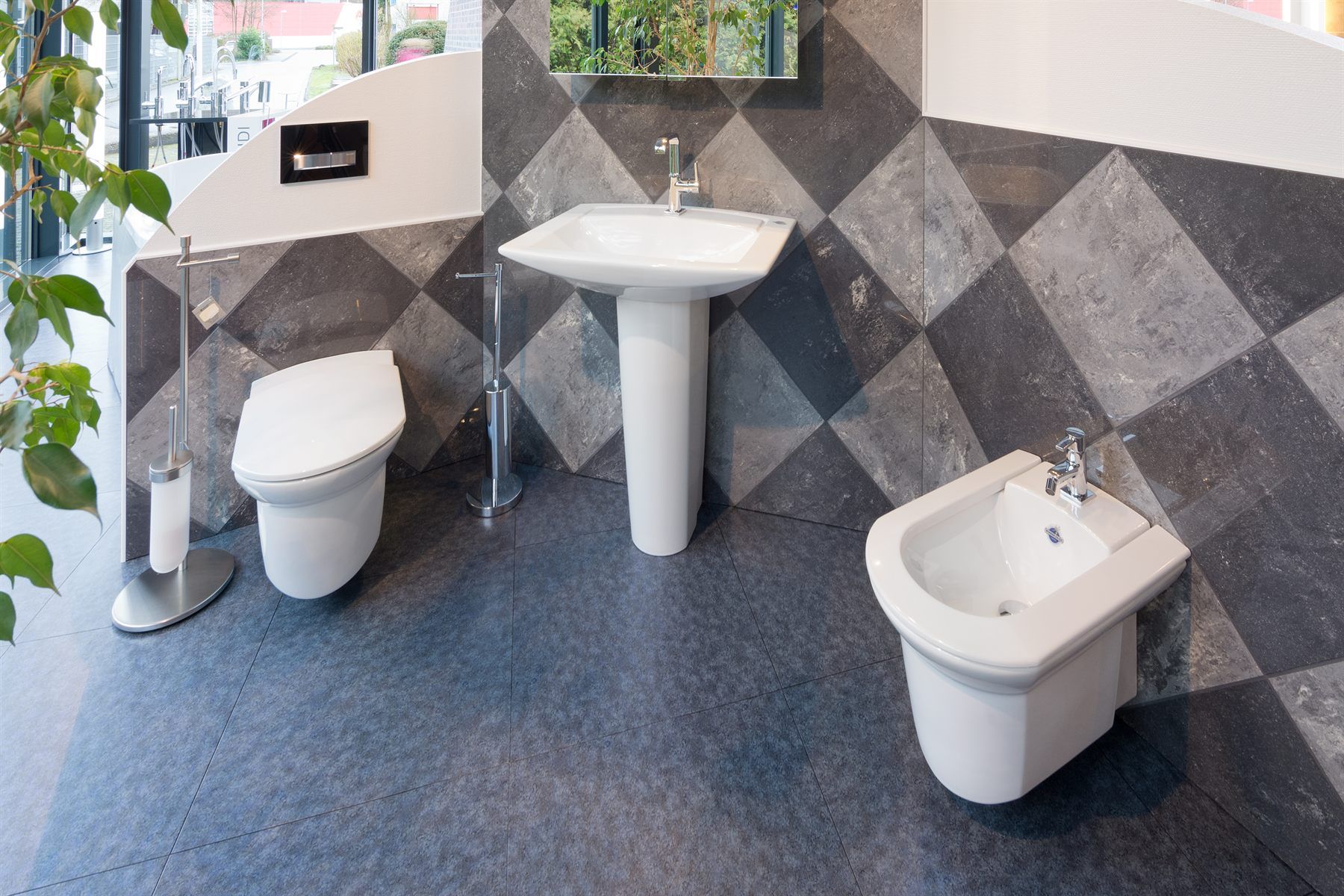Stand-WC und Bidet aus weißer Keramik vor einer Fliesenwand mit Rautenmuster